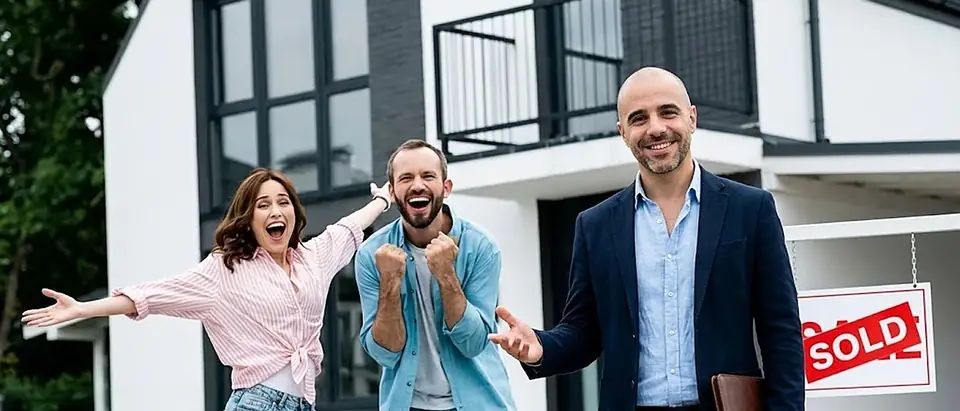 Two sellers celebrating with arms raised beside a man in front of a modern home with a SOLD sign